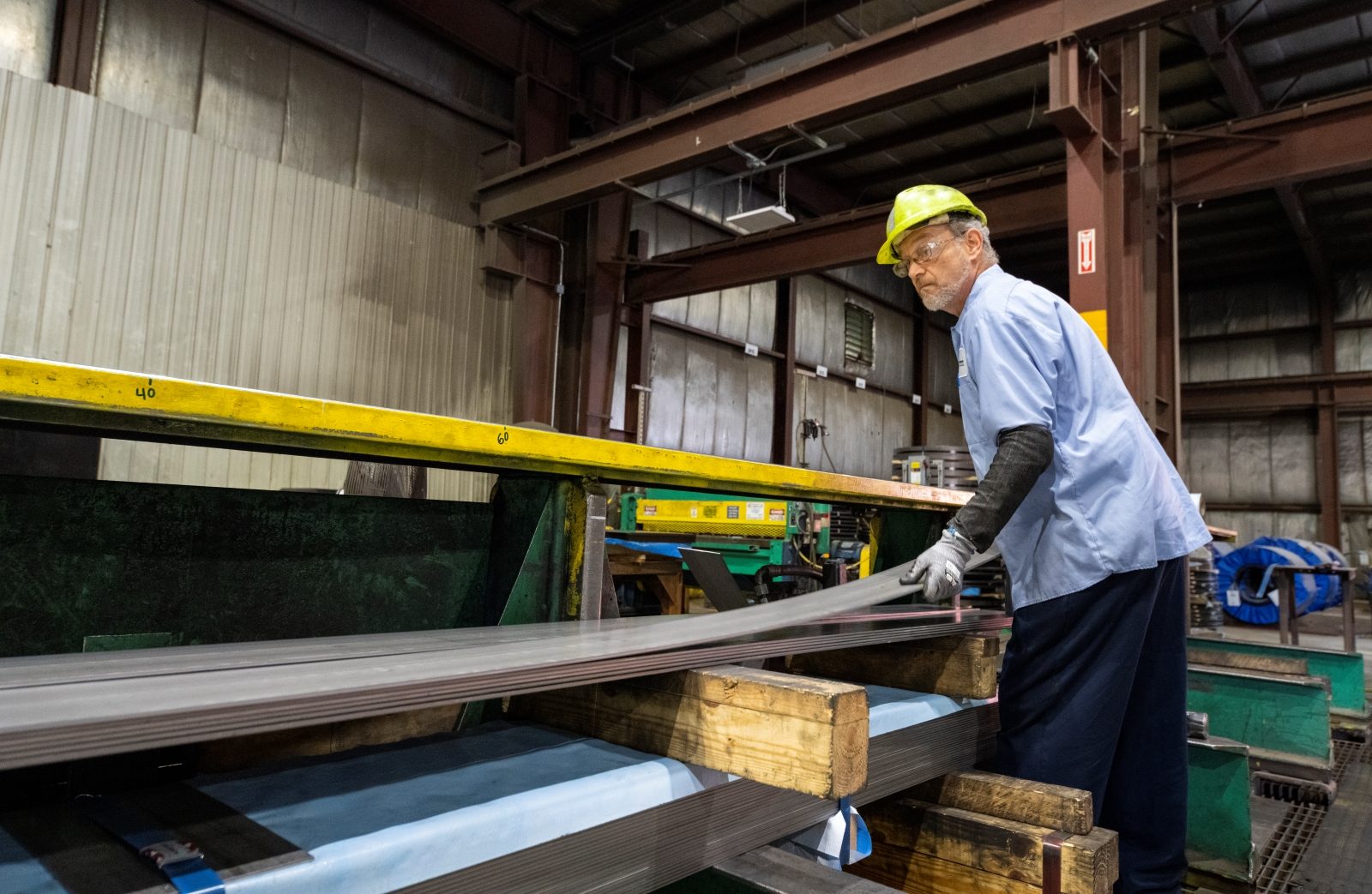 Worker in a safety helmet handling steel sheets during the cut-to-length process in an industrial facility.