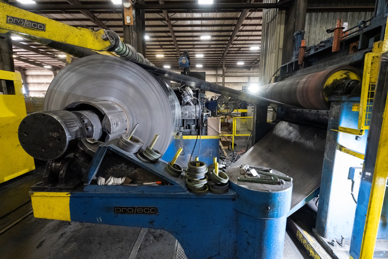 Hot rolled steel coil being processed on industrial machinery with tools and equipment visible in the foreground.