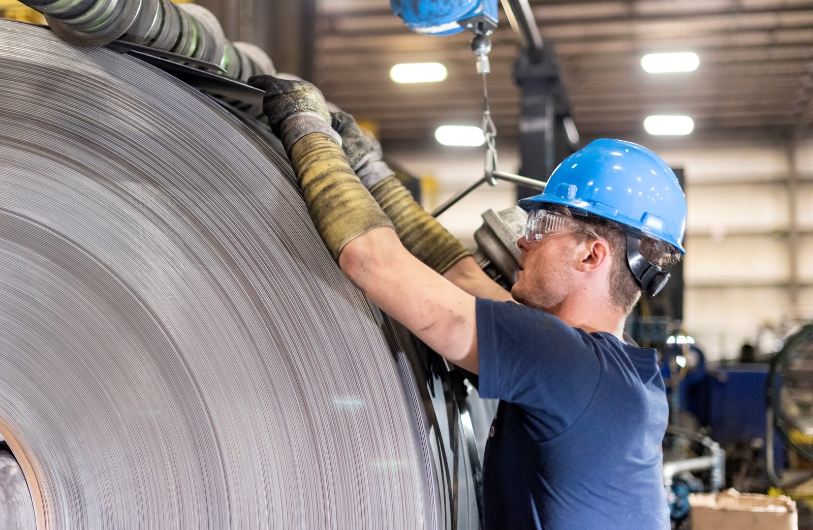 Worker in safety gear inspecting the final result of the steel edging process on a large steel coil.
