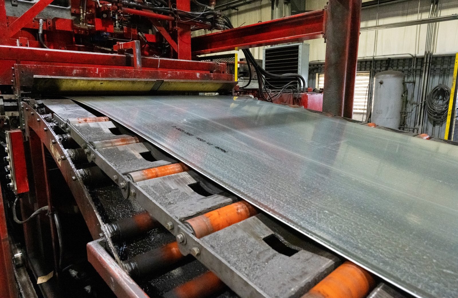 Steel sheet undergoing the leveling process on a red industrial production line, ensuring flatness and quality.