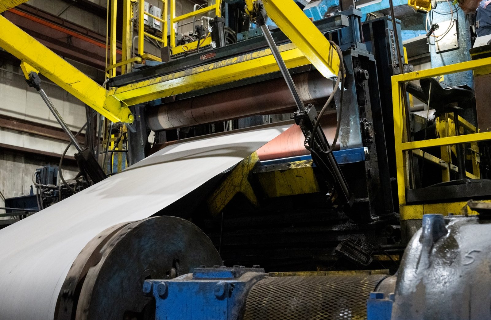 Steel sheet undergoing the tempering process on industrial machinery with yellow structural supports visible.
