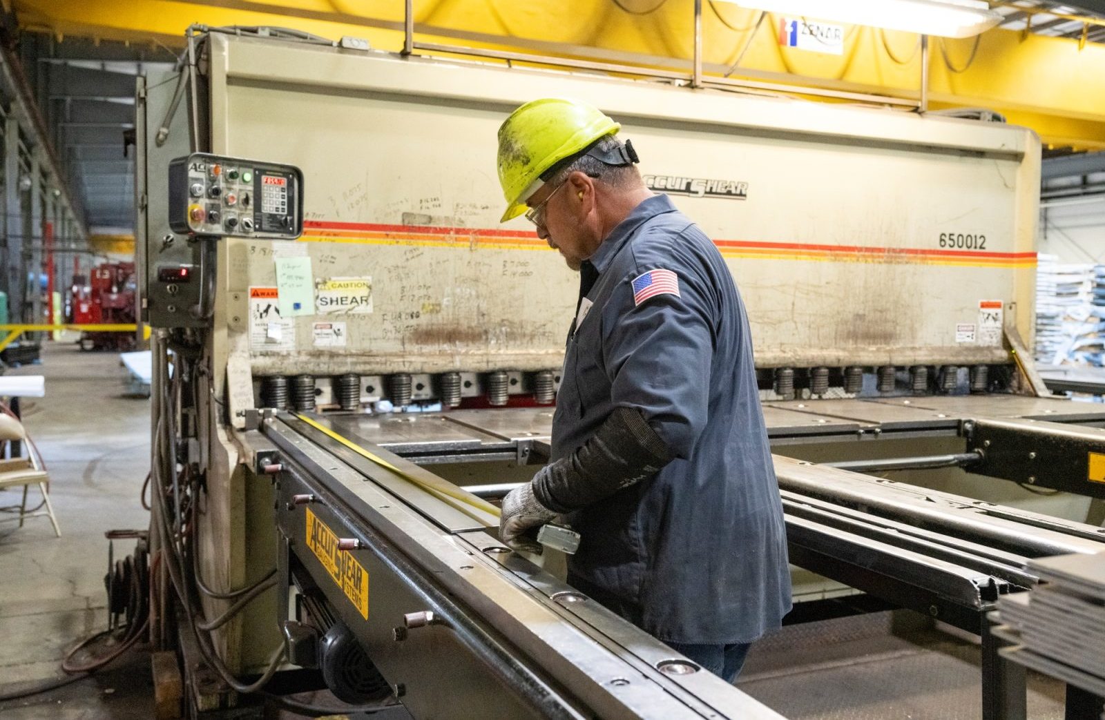 Worker in a safety helmet handling steel sheets during the cut-to-length process in an industrial facility.